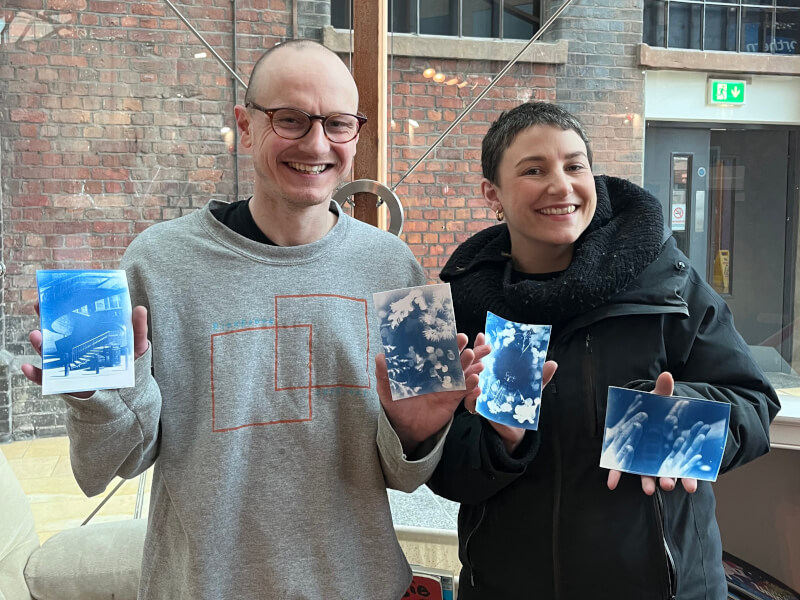 Two people hold up handmade cyanotype prints