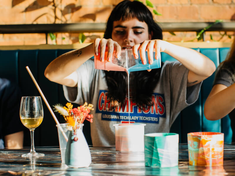 A woman is pouring blue and pink paint in a plant pot making class