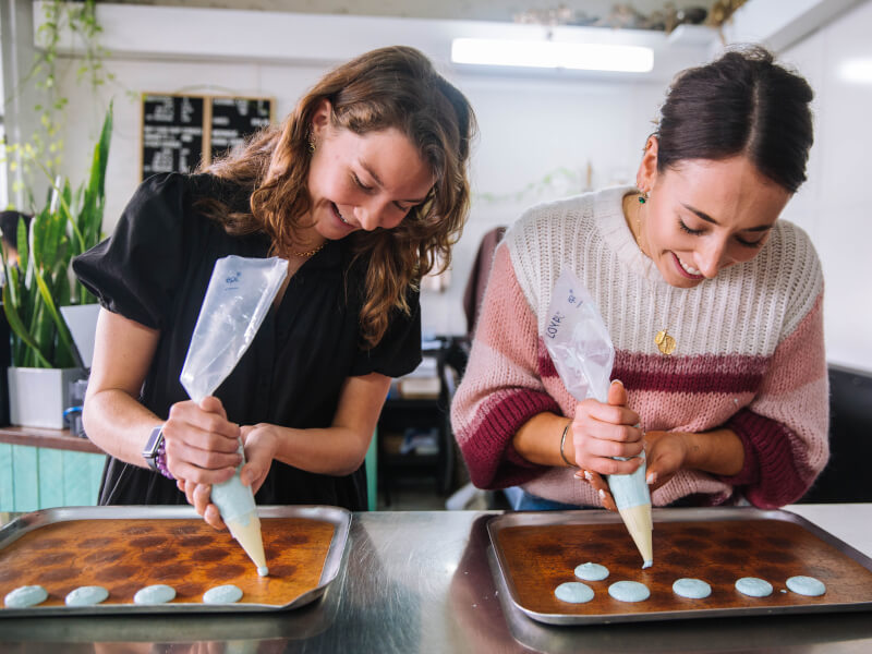 Two women are piping macarons onto baking trays ready to go into the oven