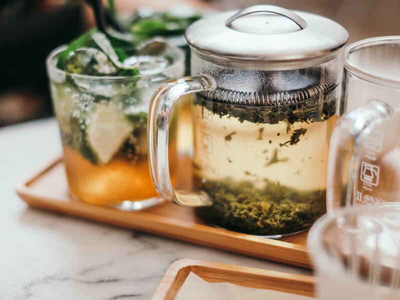 Loose leaf tea pot next to a cocktail filled with ice.