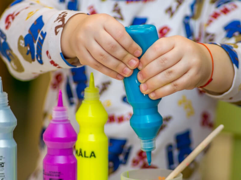 Small child's hands squeezing blue paint into a mixing cup