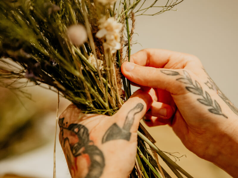 A close up of two hands with tattoos holding a bunch of dried flowers