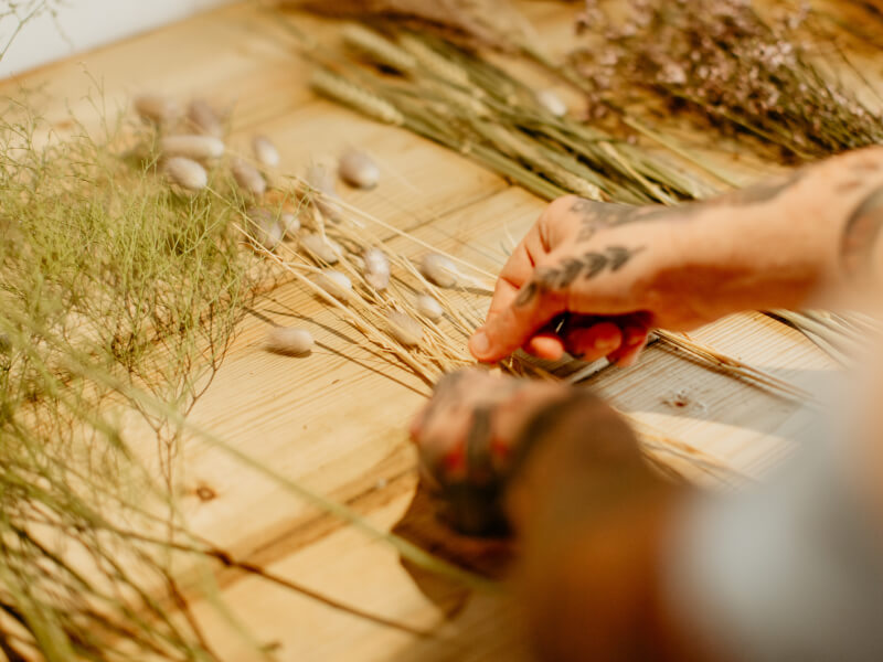 A close up of someone arranging dried flowers into a bouquet on a wooden table