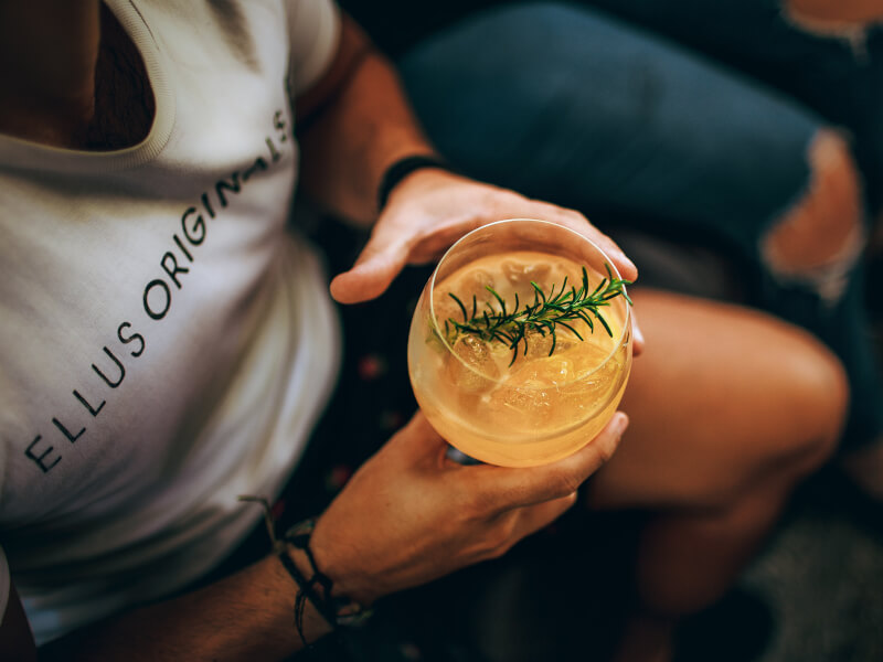 Man holding DIY cocktail garnished with a sprig of rosemary.