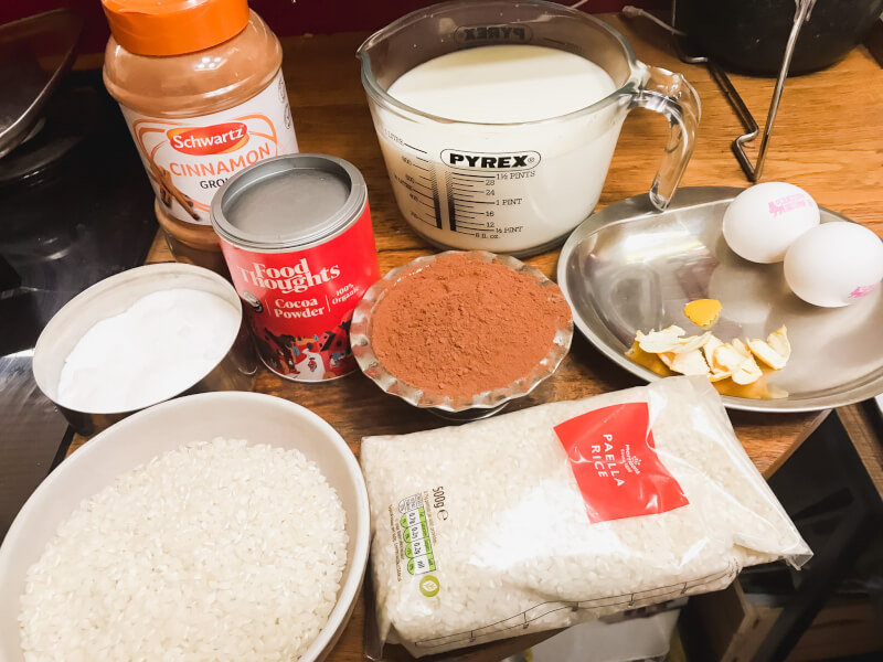 A table full of ingredients including rice, cocoa powder and milk to make Spanish chocolate rice cake