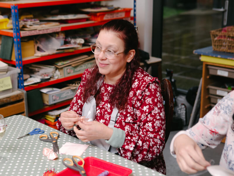 A woman is hand sewing a piece of red patterned fabric