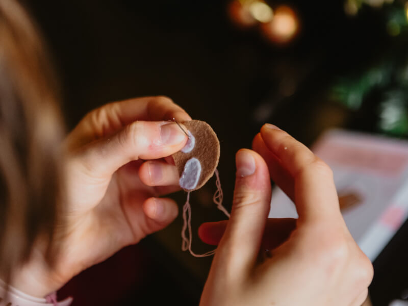 A close up of a person sewing felt shapes using a needle and thread