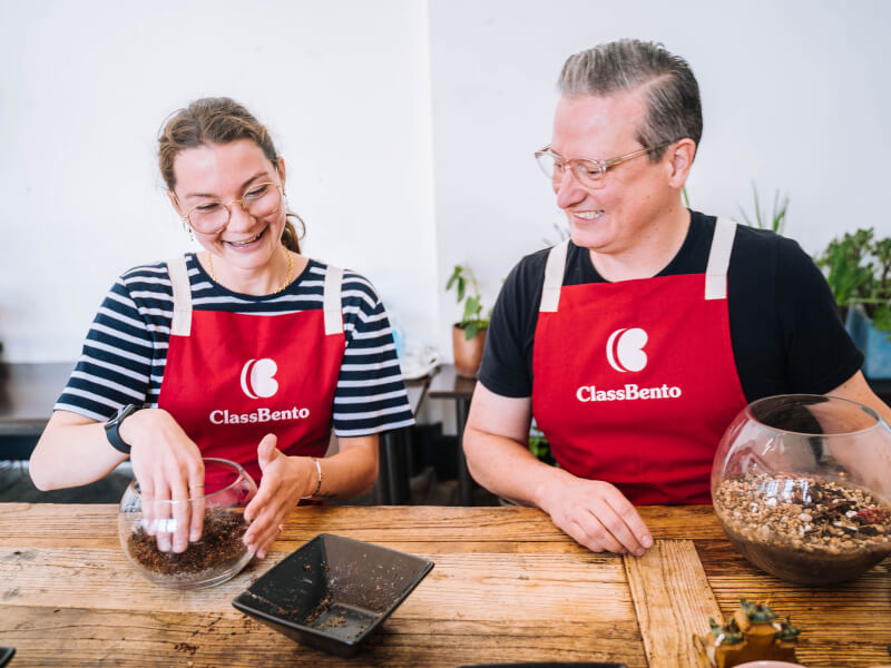 Woman and man smiling while building terrariums in a terrarium class.