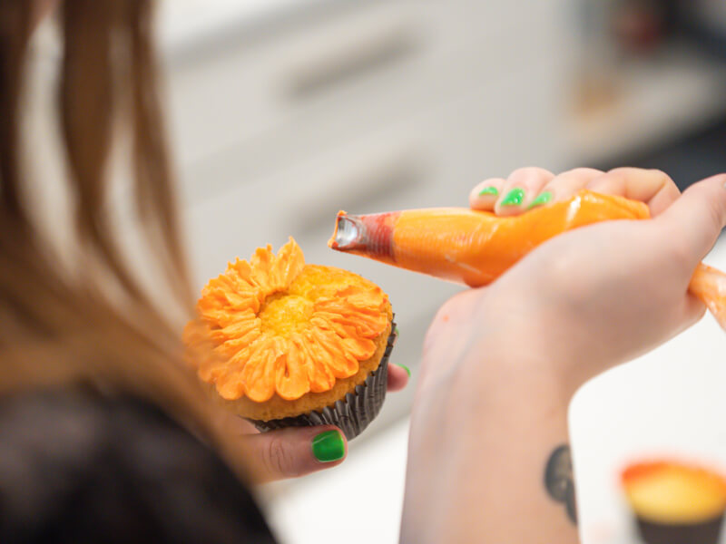 A person is decorating a cupcake with orange frosting