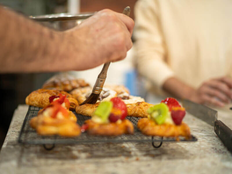 A close up of a person glazing pastries on a wire rack