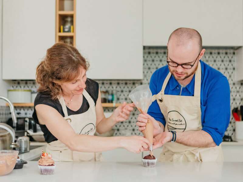 Two people at a baking class are decorating a cupcake with chocolate frosting