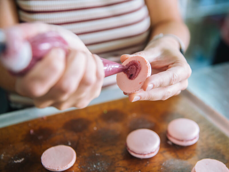 A person is piping the centre into pink macarons
