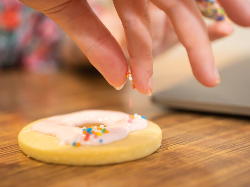 A person is adding sprinkles to an iced biscuit