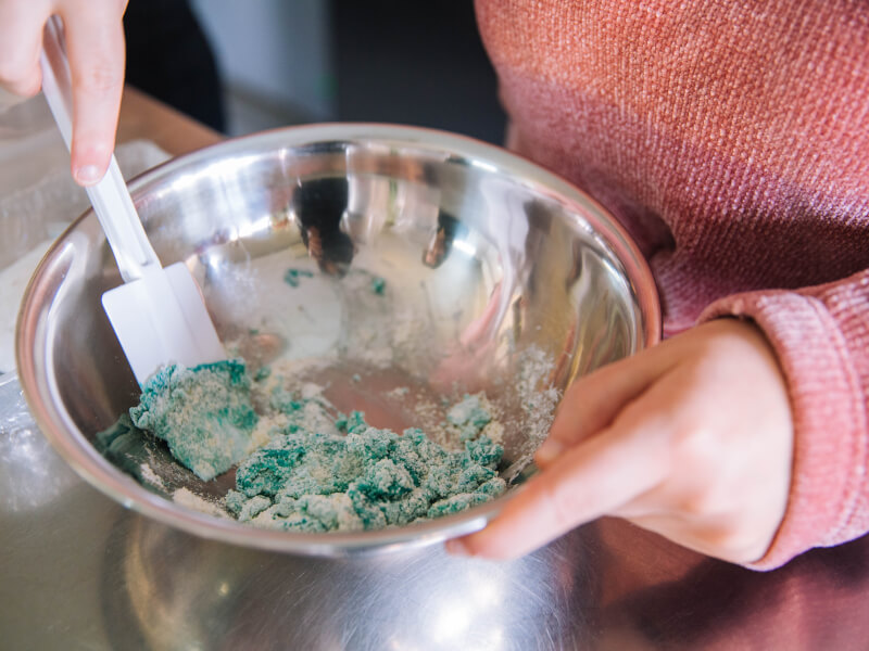 A person is stirring a bowl with blue dough in it