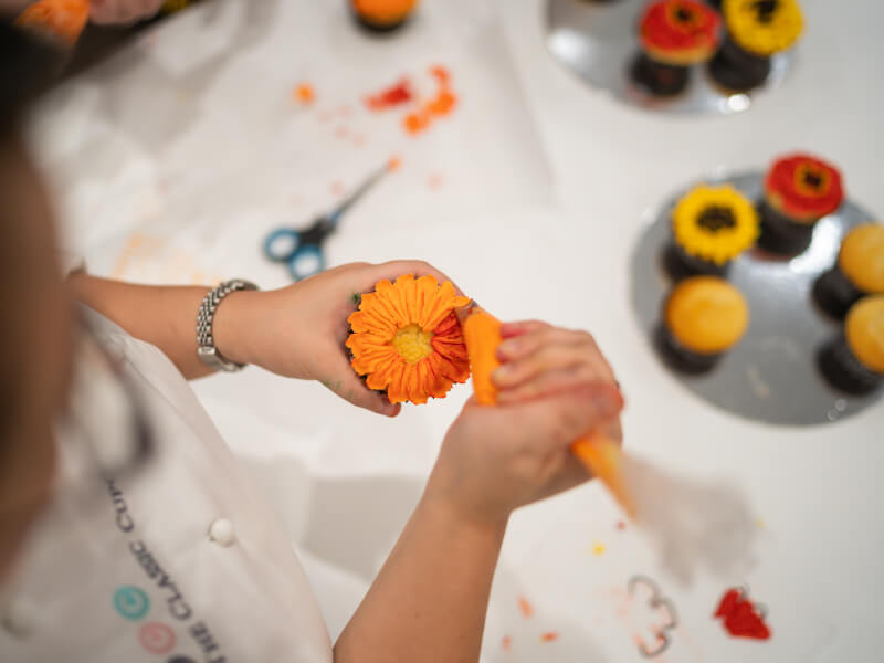 A close up of a person decorating a cupcake with bright orange frosting