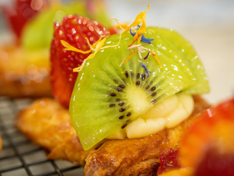 A close up of a selection of handmade pastries topped with fruit sitting on a wire rack
