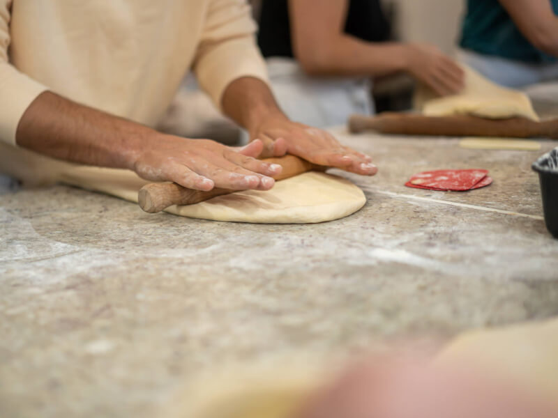 A person is rolling out dough with a wooden rolling pin on a floured worktop