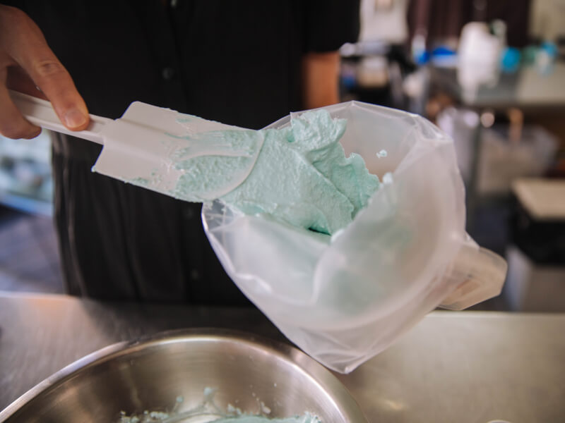 A close up of a person mixing blue mixture in a bowl