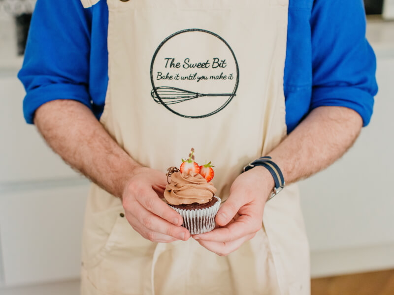 A close up of a person holding a hand decorated cupcake topped with strawberries and chocolate embellishments