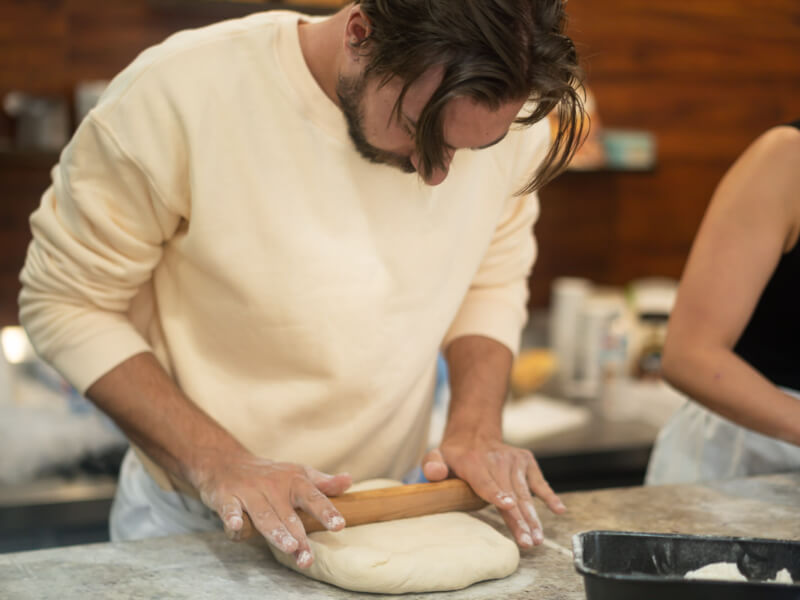 A man is rolling out dough with a rolling pin on a worktop