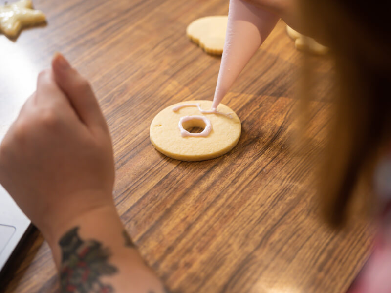 A person is icing a biscuit with pale pink icing