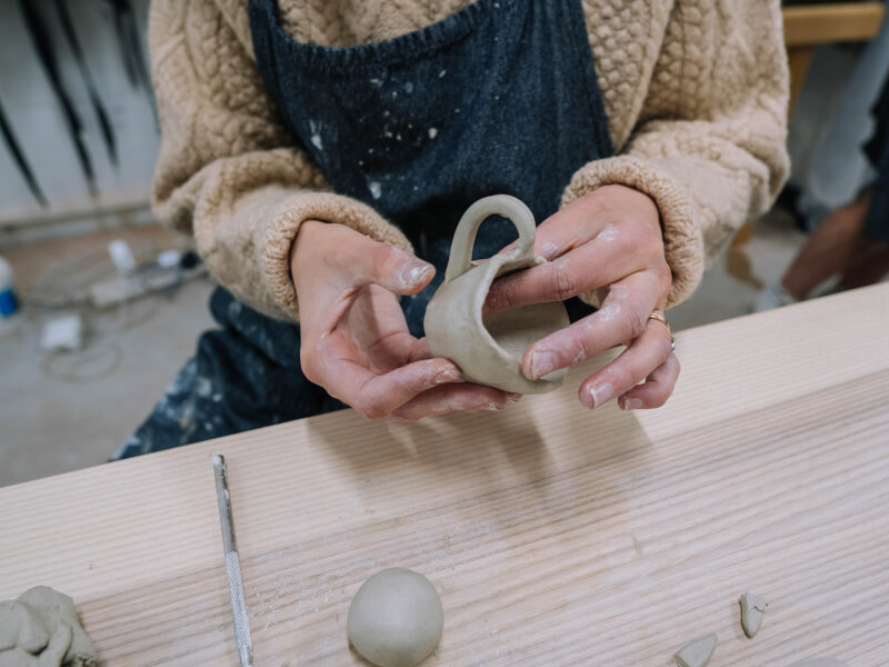 A person is adding a handle to a clay cup at a hand building class