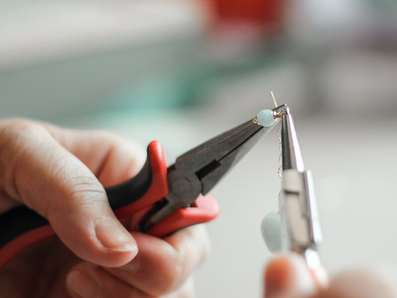 A closeup of DIY earrings held in a pair of pliers. 