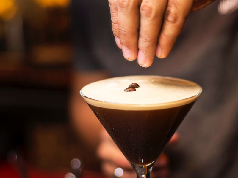 Coffee beans being added to an espresso martini cocktail at home.