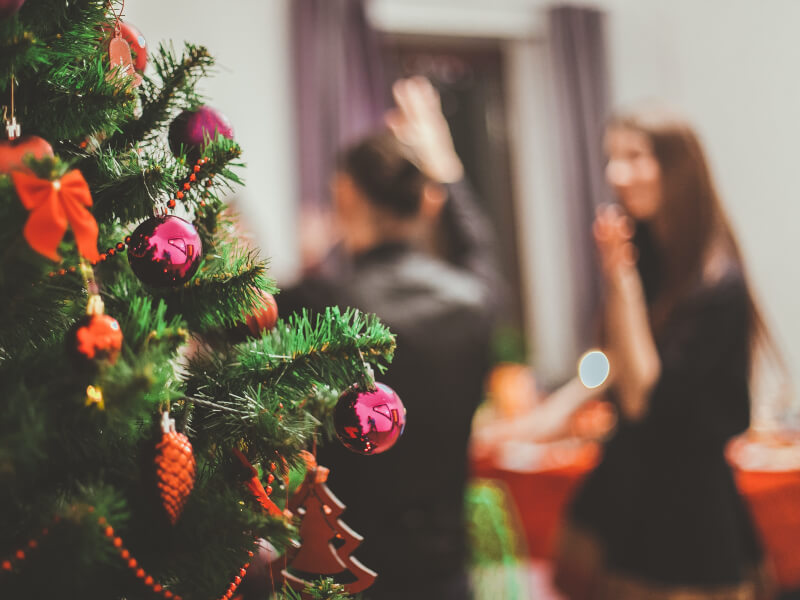 A Christmas tree sits in the forefront whilst people dance in the blurred background.