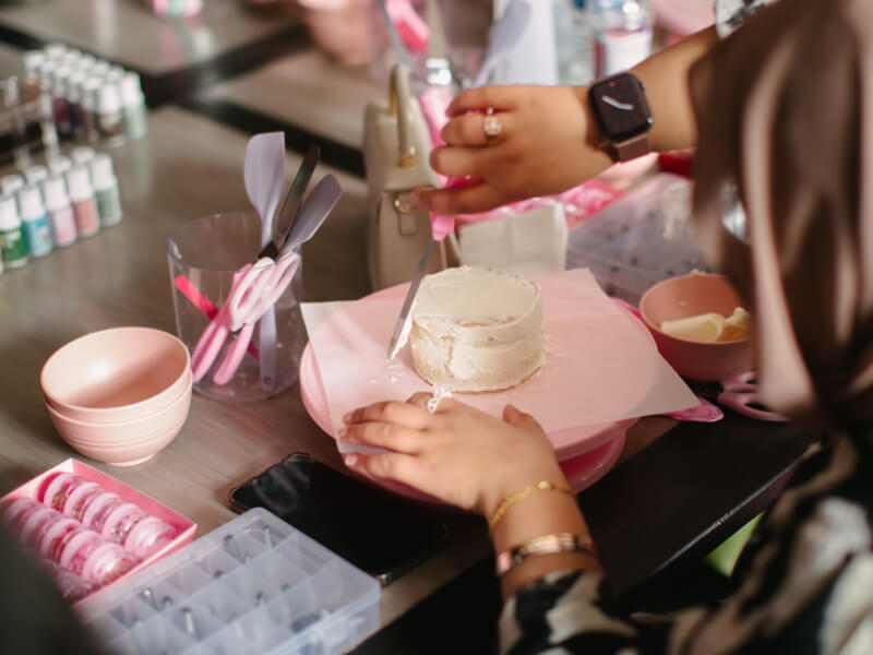 A close up of someone decorating a small sponge cake with white buttercream icing