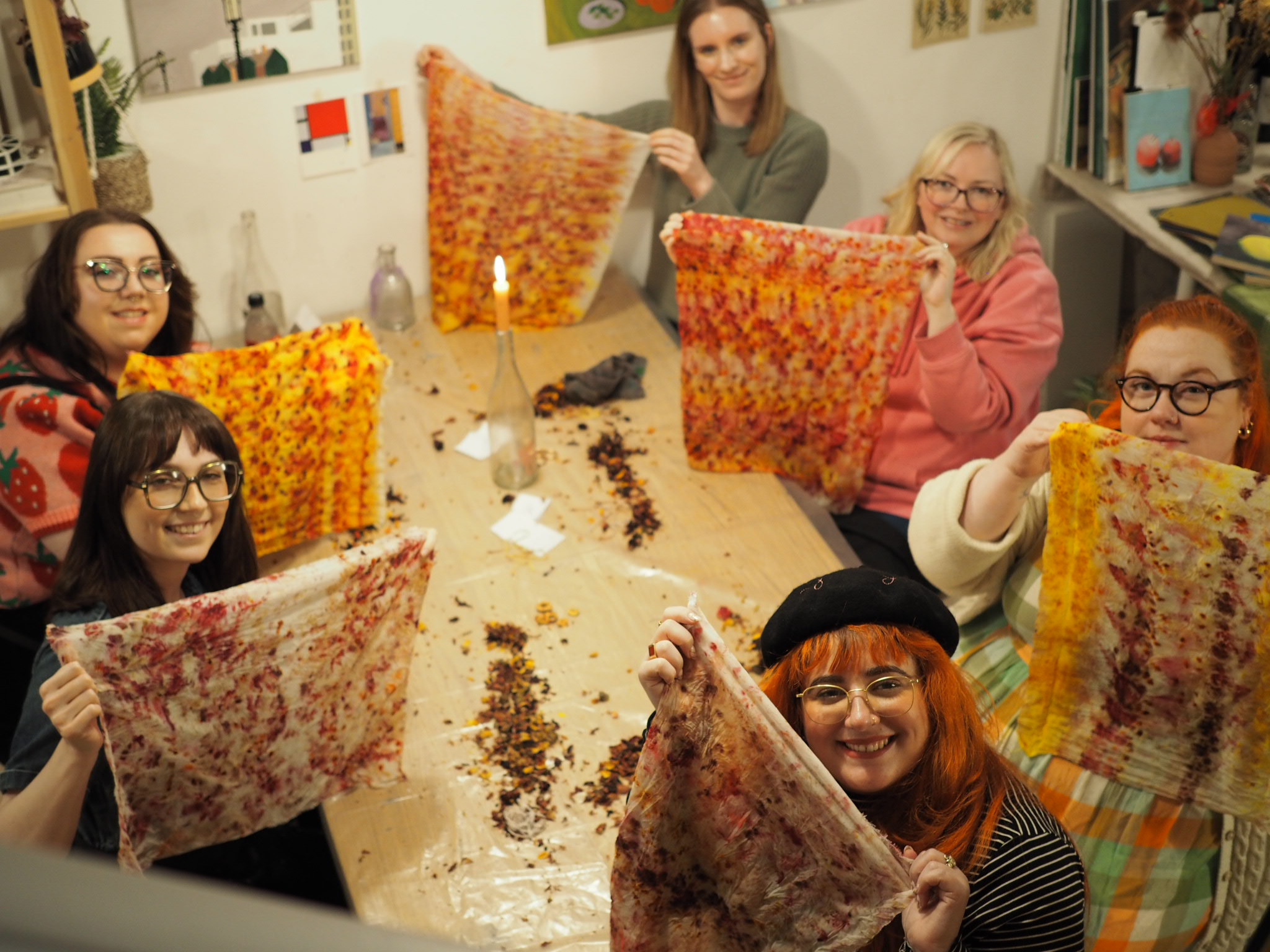 A group of people holding up fabric dyed with plants and foliage
