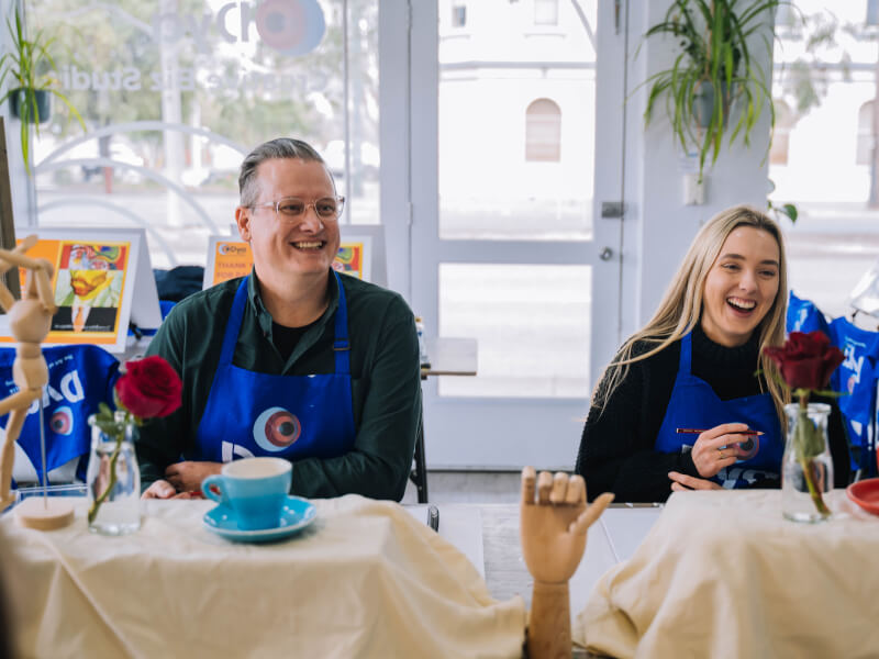 A man and woman are sitting at a table at an art class sketching