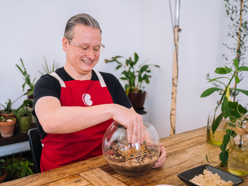A man is sitting at a table, making a glass terrarium