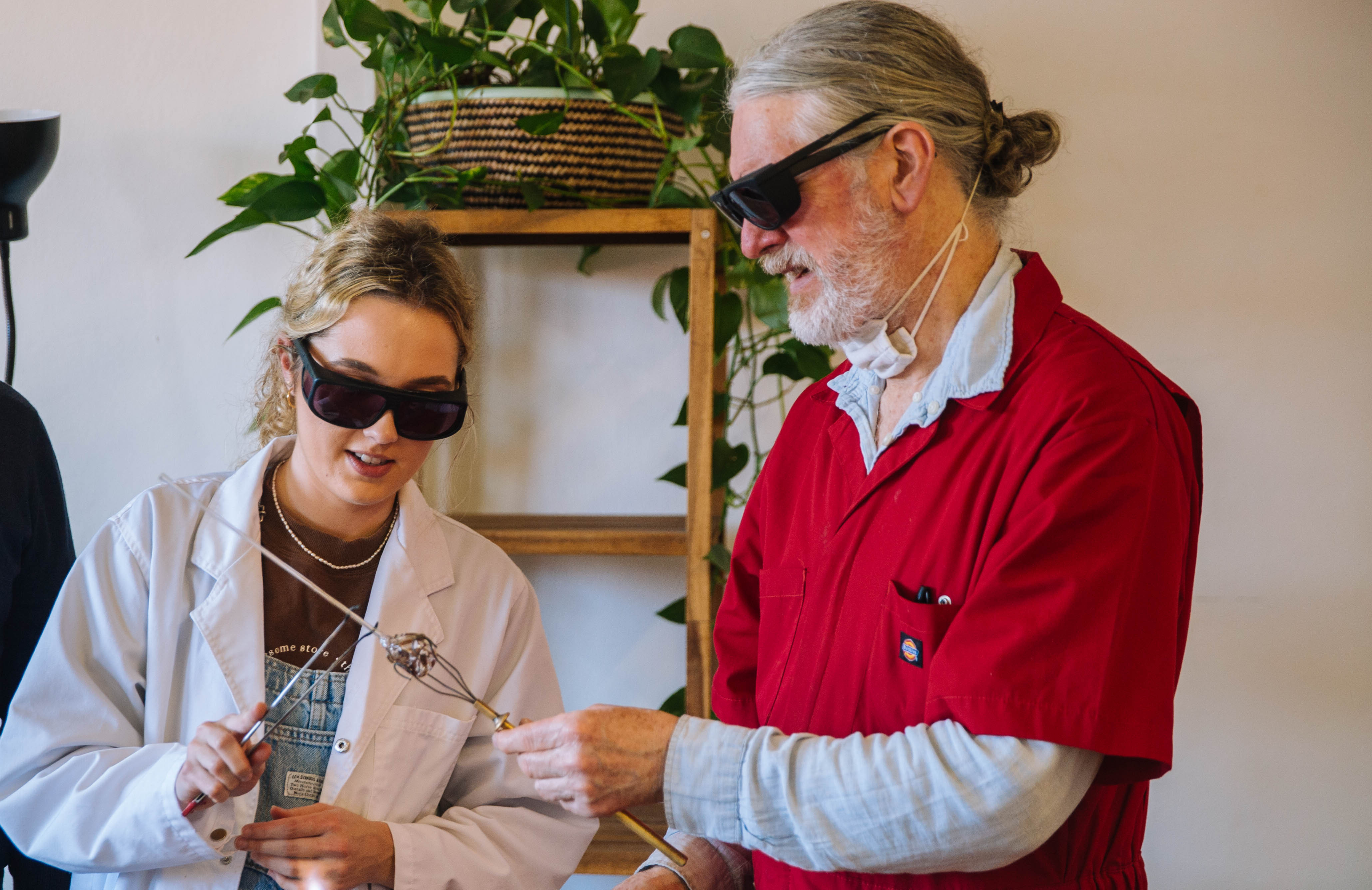 A man and woman are shaping molten glass with special tools