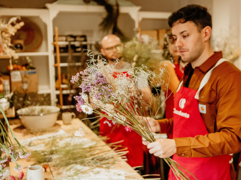 A man is making a hand tied bouquet of dried flowers at a floristry class in Brighton