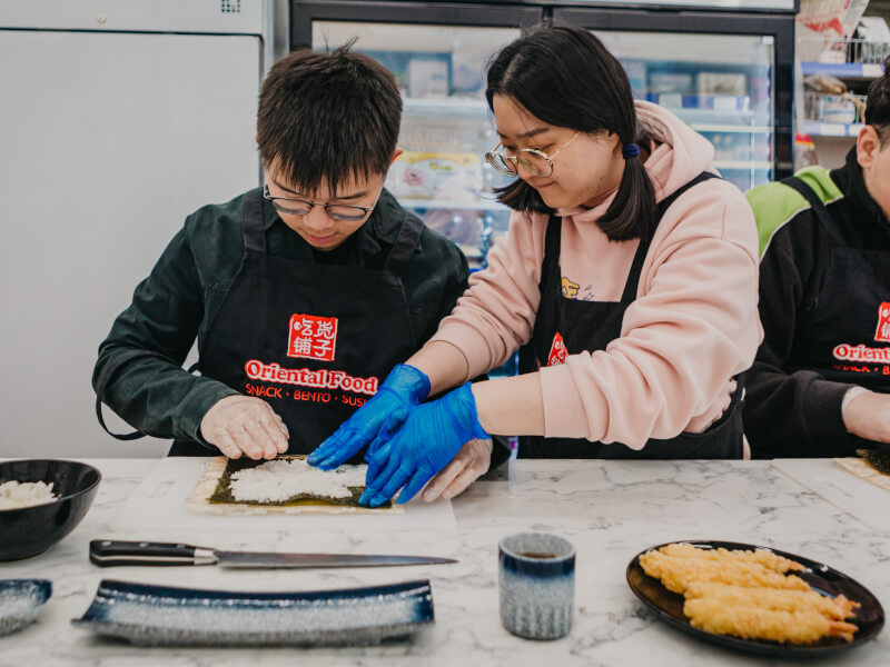 A woman is teaching a man how to roll sushi at a marble table