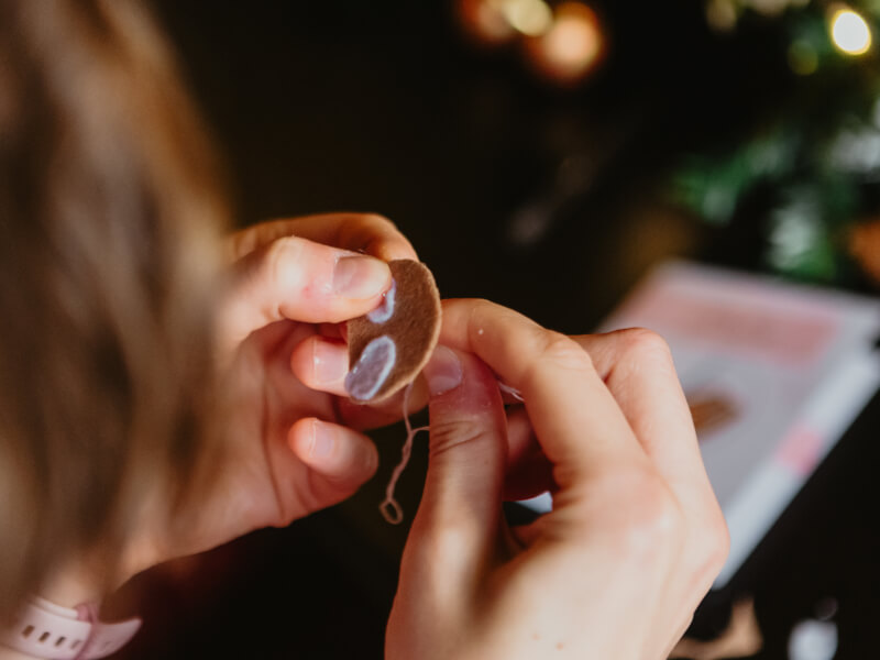 A close up of a person hand sewing felt shapes into a sloth face