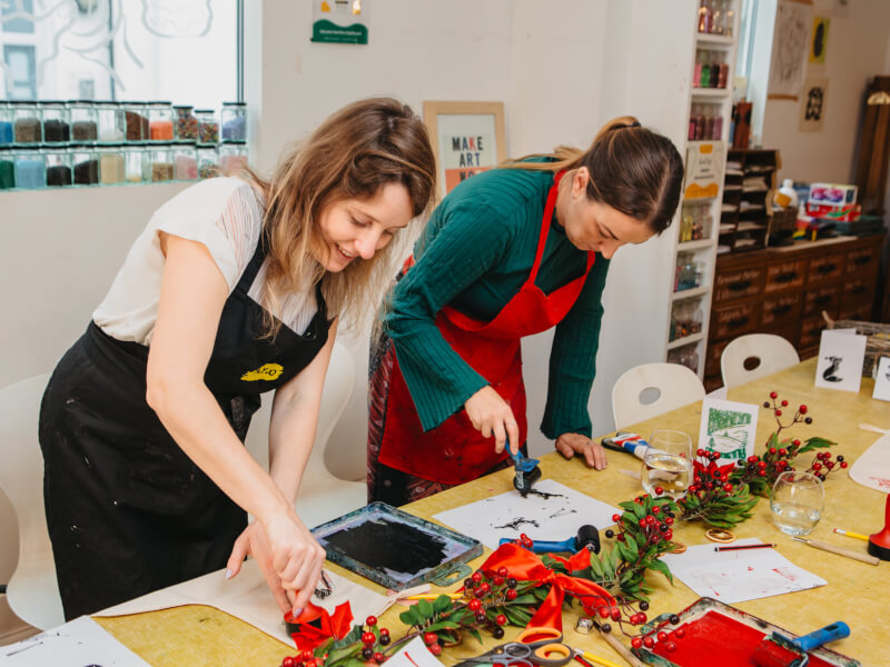Two women are inking stamps at a Christmas lino printing class