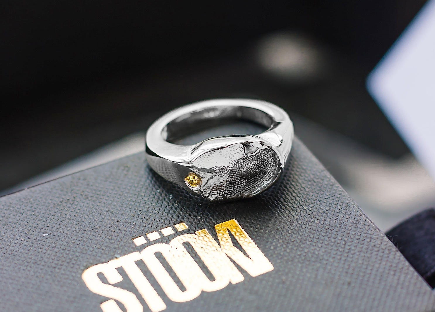 A silver ring with a fingerprint and a gem on a box. 