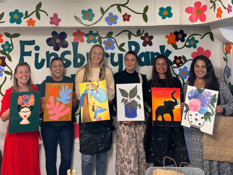 Six women hold their finished paintings at Finsbury Park Painting Club