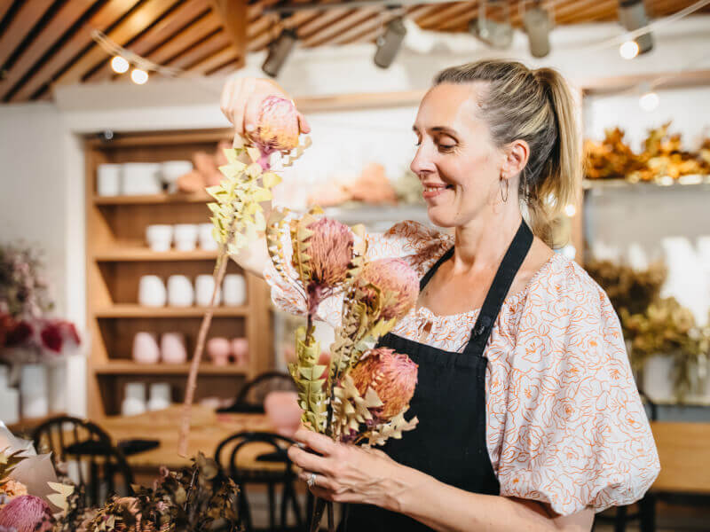 A woman is smiling and putting pink flowers in a vase