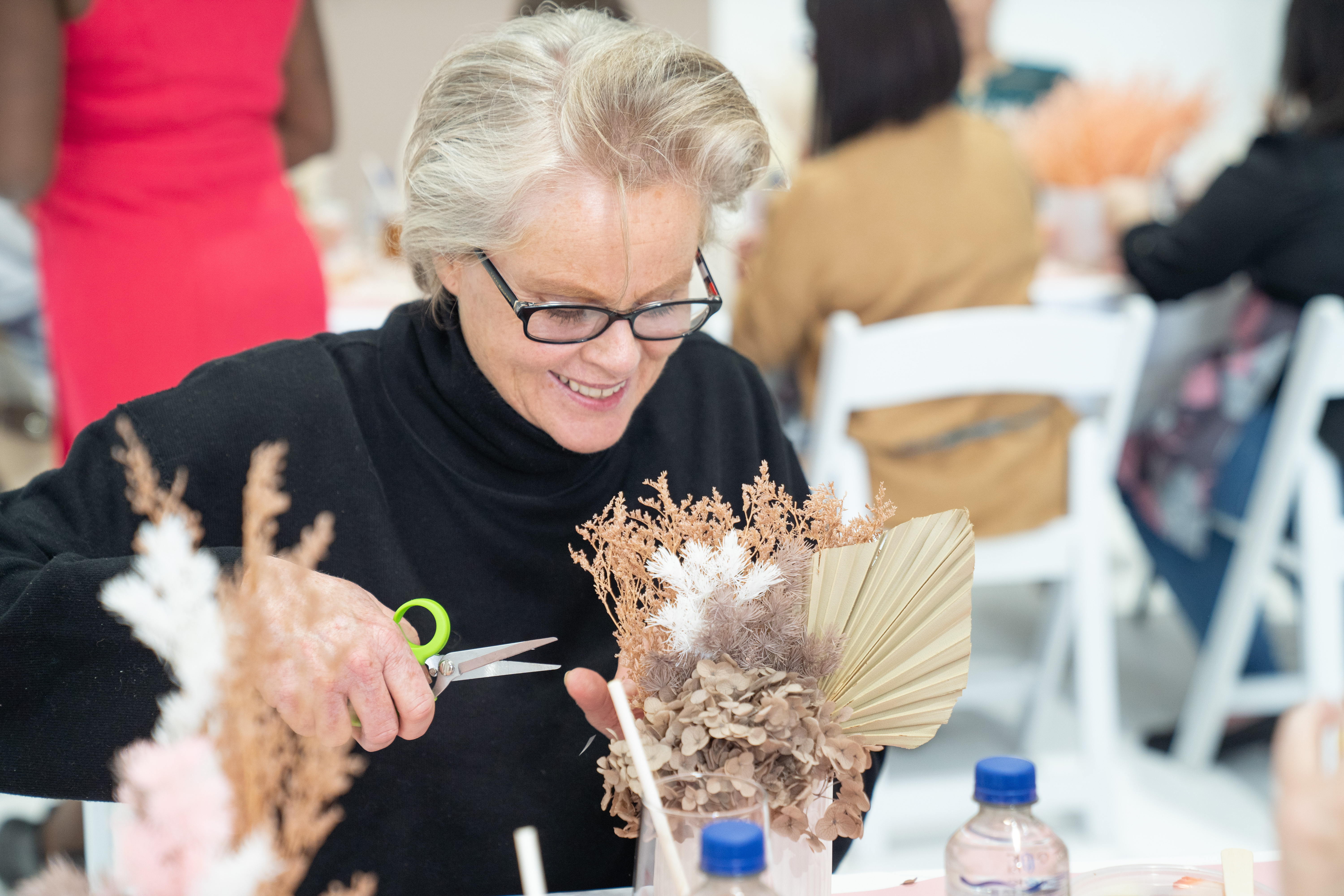 A woman is trimming dried flowers for an arrangement