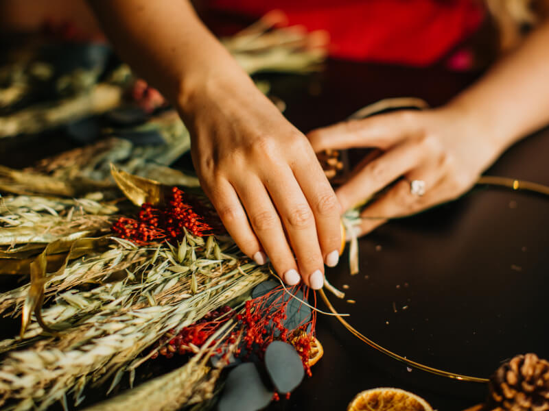 A hand arranging dried flowers into a wreath. 