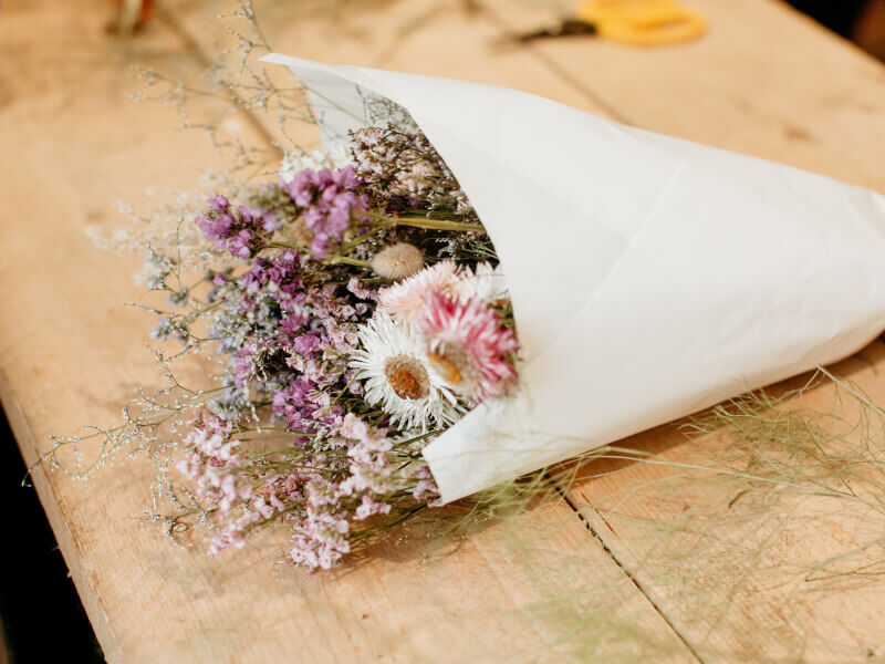 A bouquet of flowers wrapped in white paper sits on a table