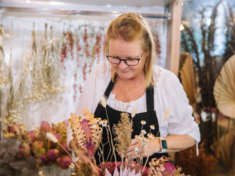 A woman is standing at a table, creating a floral arrangement in a vase