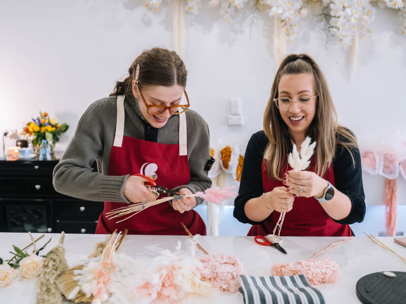 Two women are creating floral arrangements from dried flowers