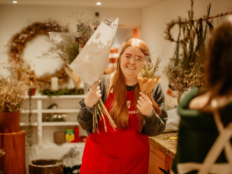 A woman smiles and holds a large dried flower bouquet and a small dried flower bouquet