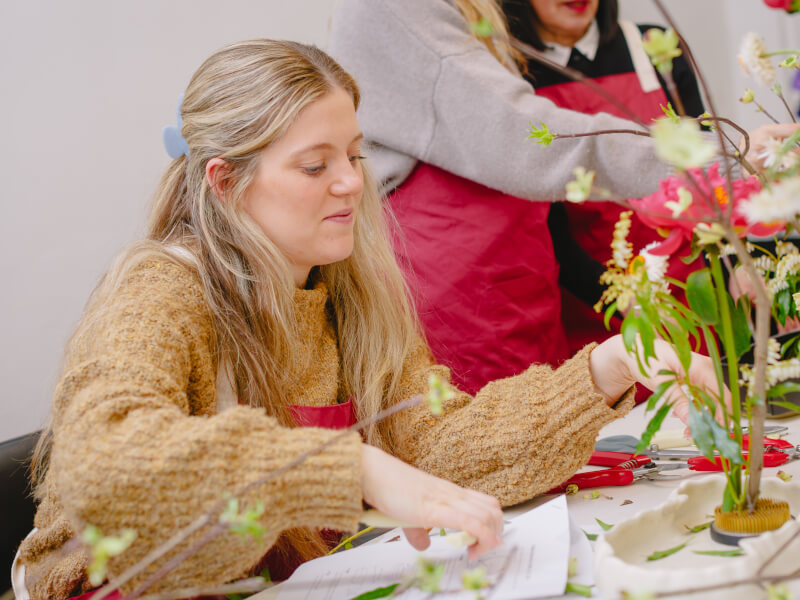 A woman is sitting at a table making a floral arrangement