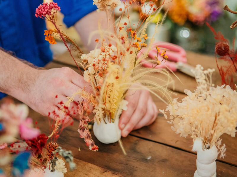 A close up of a person arranging flowers into a ball of clay