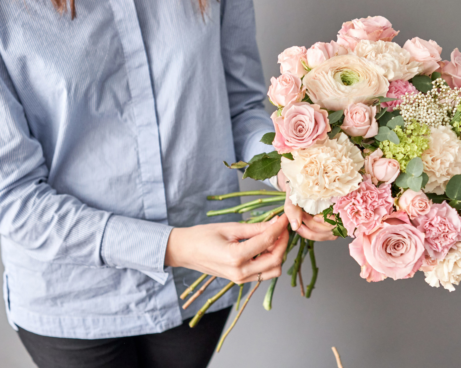 A person in a blue shirt is holding a large bunch of pink flowers and green foliage